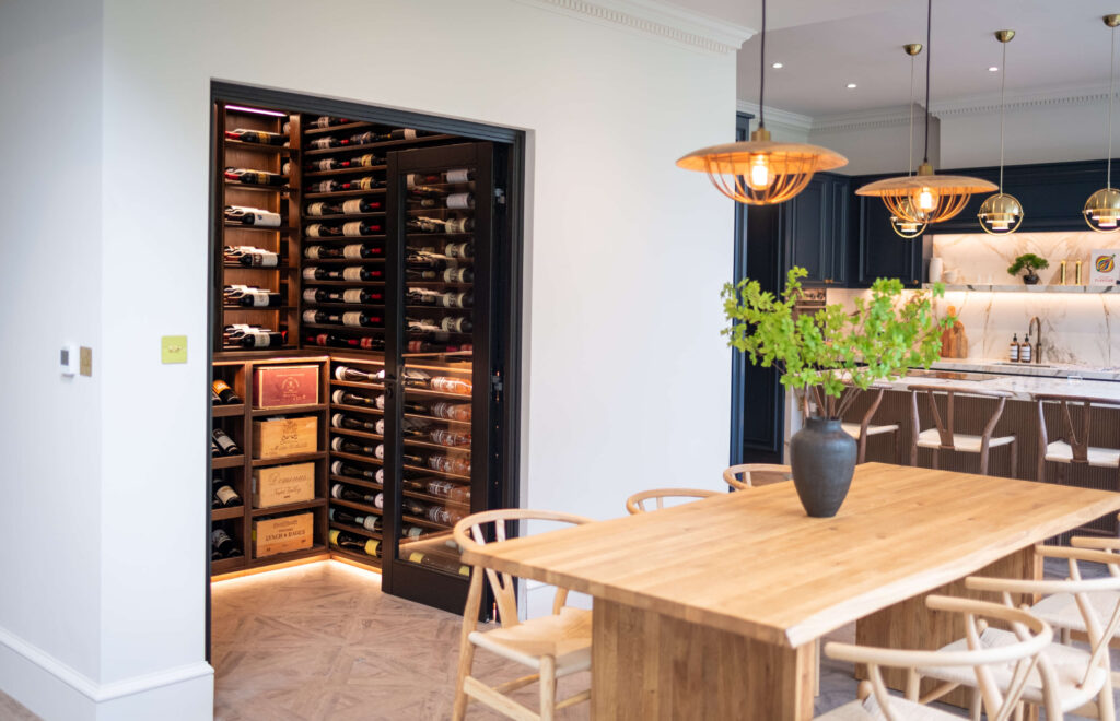 A kitchen with a Sorrells wine room located within. The dark wood wine room compliments the rest of the kitchens wooden interior hues and scandi style.