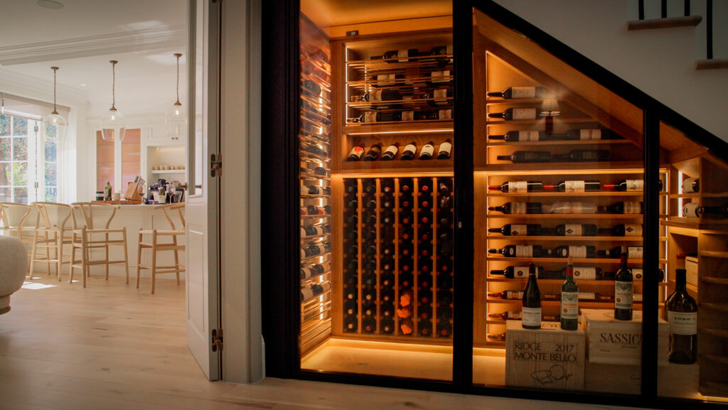 Temperature-controlled wine cellar beneath a staircase featuring oak wine racking and black metal detailing
