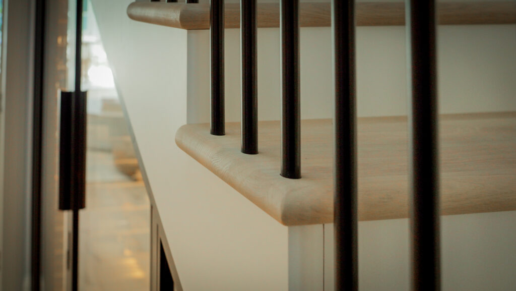 Luxury residential wine cellar designed under the staircase with oak joinery and black steel doors